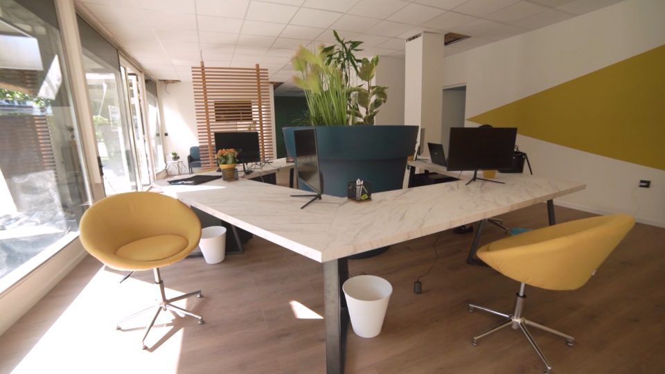 Grande table de travail en marbre blanc avec chaises jaunes dans un espace de coworking lumineux à Pau.